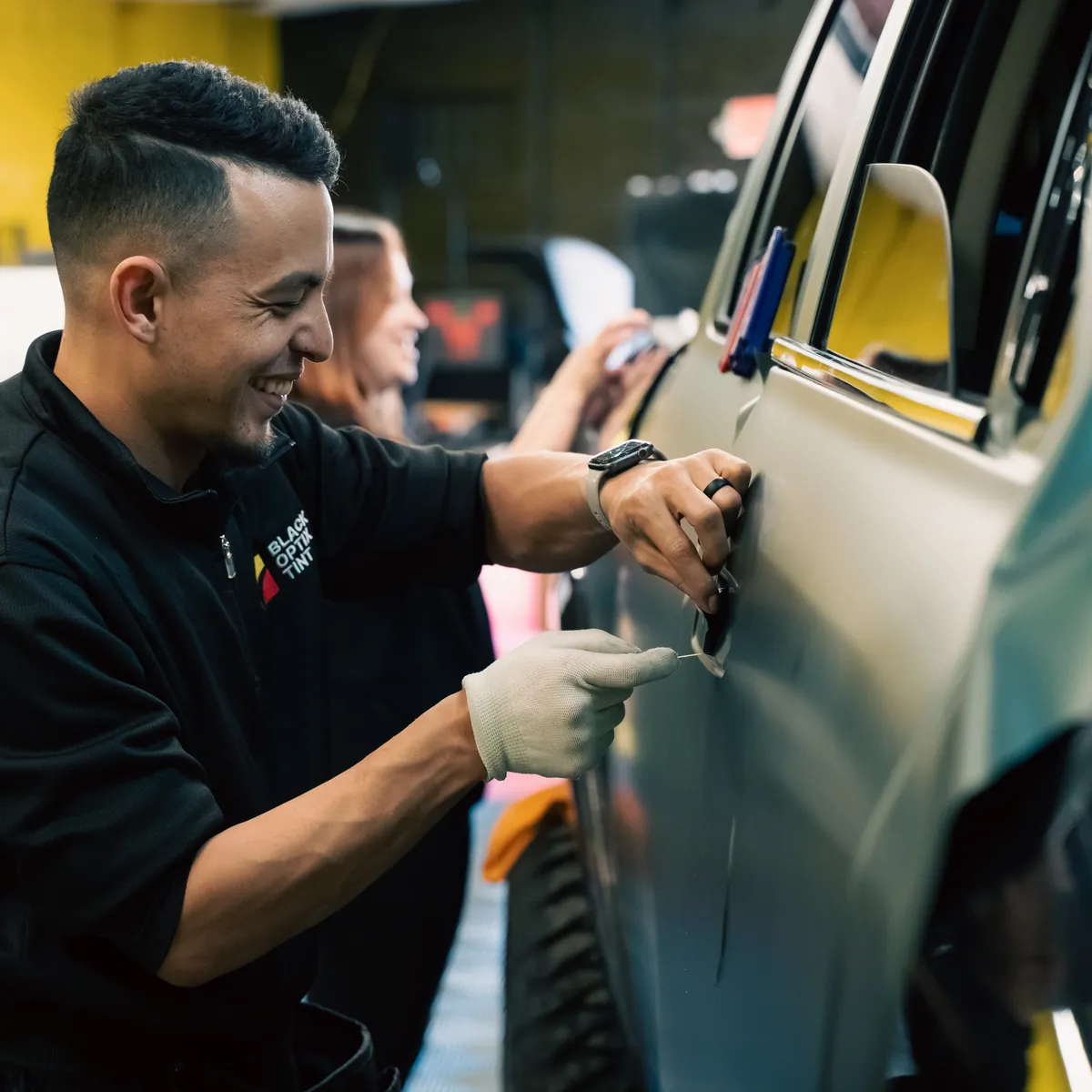 Black Optix Tint technician trimming window film on a car door